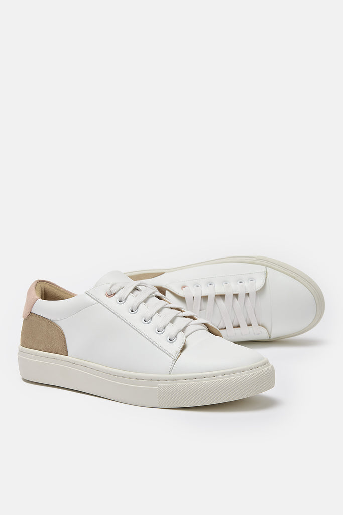 pair of white vegan leather trainers with gold and pink heel detail- one trainer is shown on its side