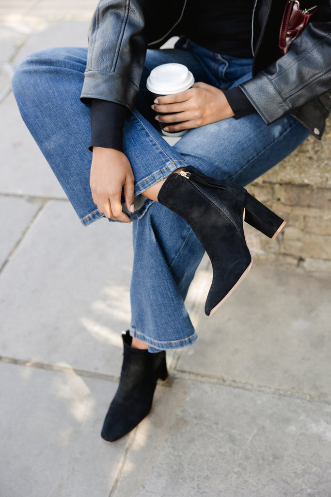 Person wearing blue jeans and black ankle boots, holding a white cup.