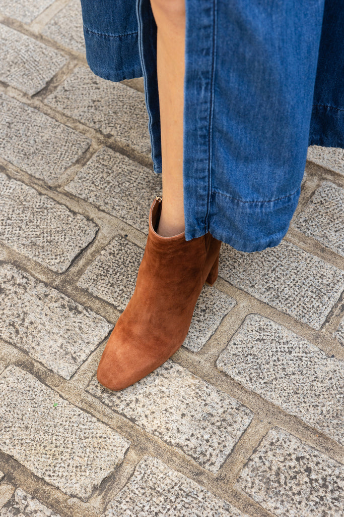 Brown ankle boots worn with blue jeans on a stone pavement