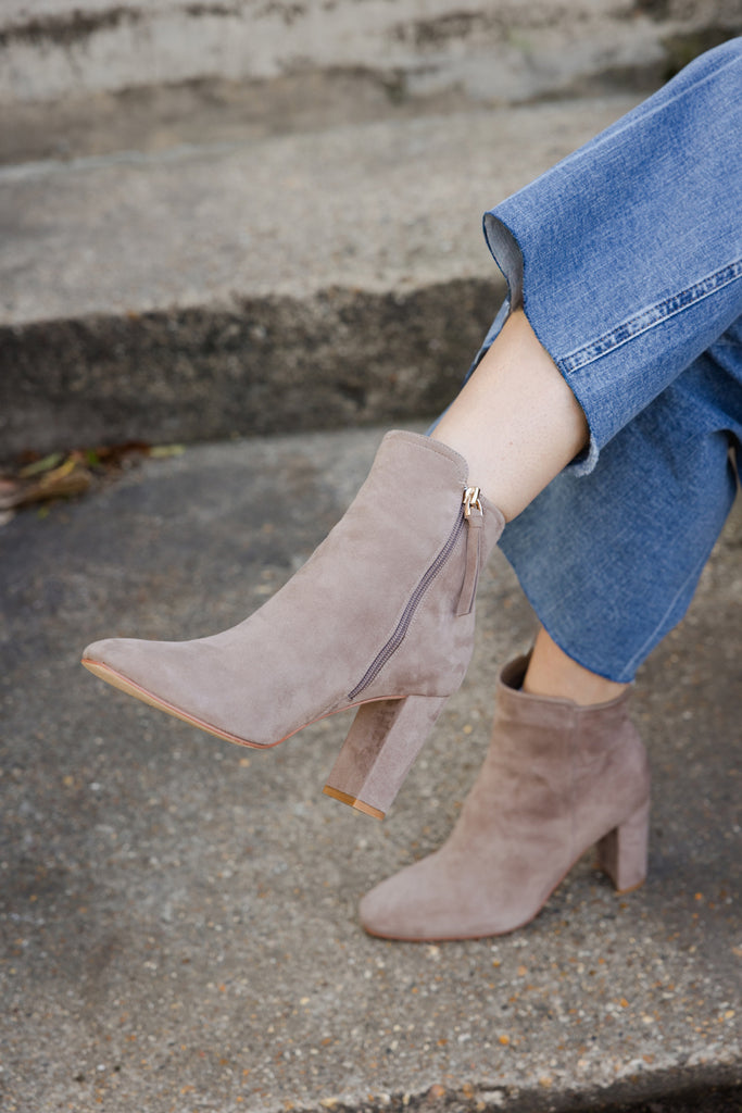 Taupe suede ankle boots worn with jeans on a concrete surface.