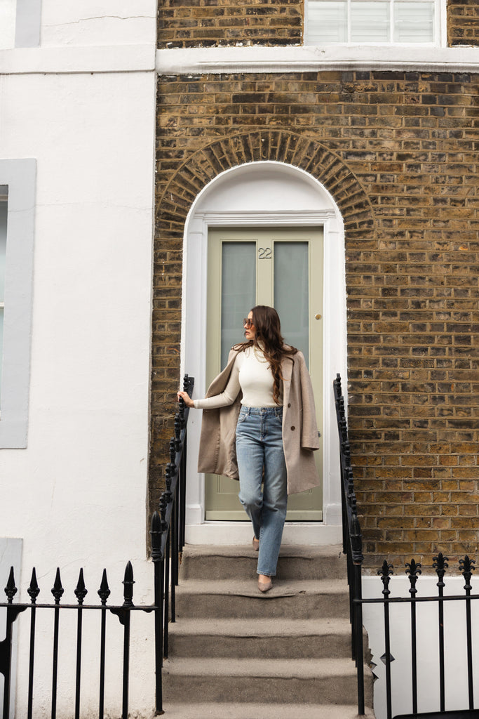 Woman standing on a set of stairs in front of a brick building with a white door.