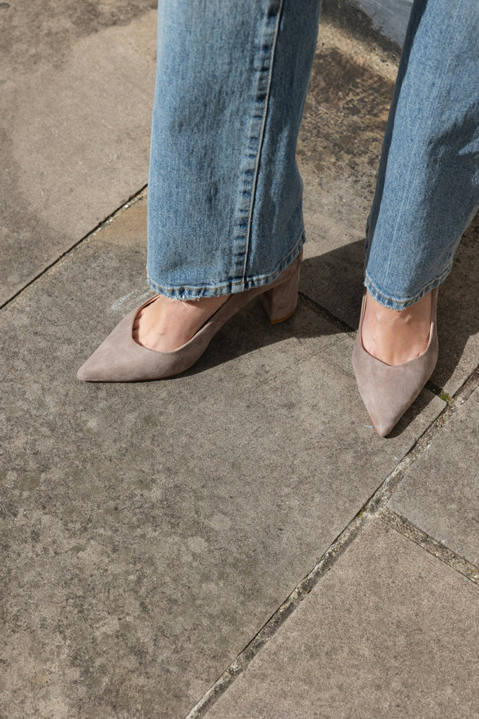 Close-up of taupe pointed-toe shoes and light blue jeans on a concrete surface