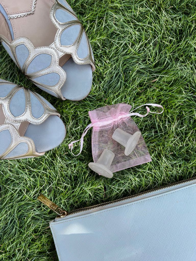Butterfly-shaped shoes on grass with a pink drawstring bag.