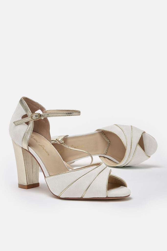 pair of ivory suede wedding shoes with gold block heel and ankle strap- one shoe is lying on its side