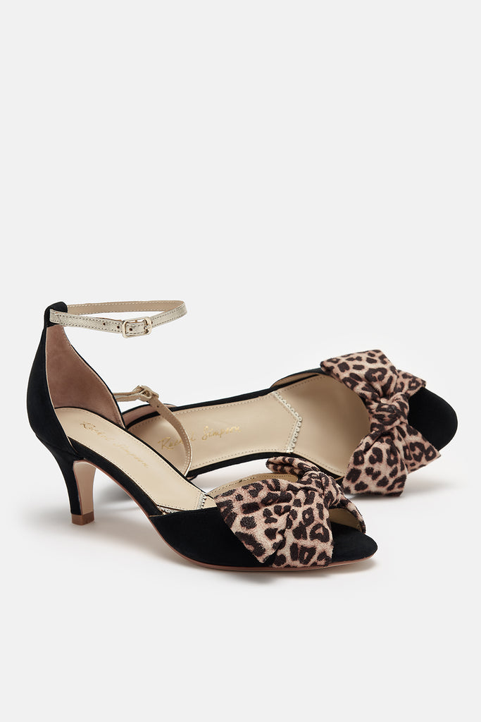 pair of black suede low heel two part occasion shoes, with oversized leopard bows and gold leather ankle straps- one shoe is lying on its side