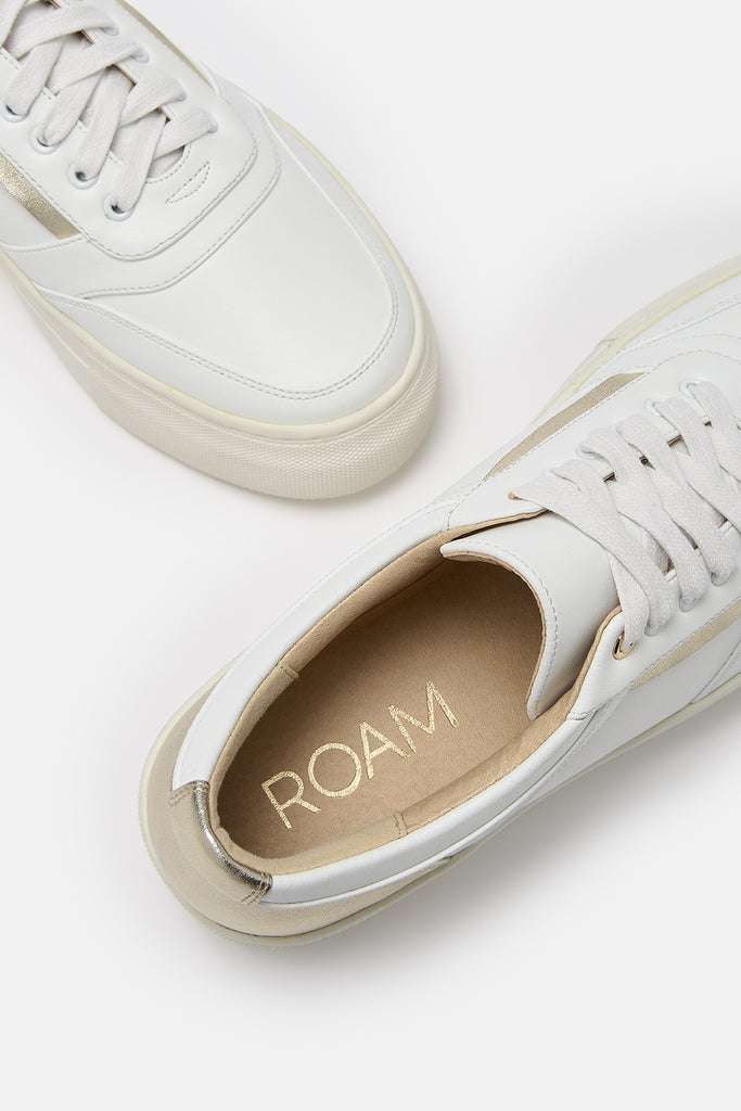 Close up shot of a pair of white and gold vegan leather trainers.