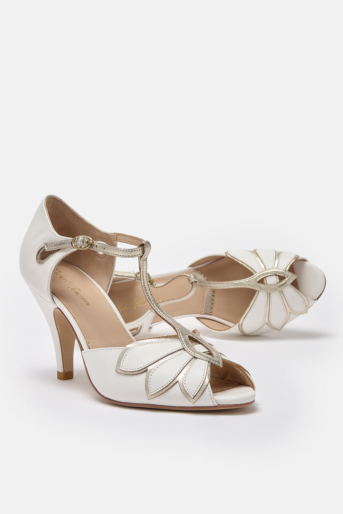 pair of ivory leather and gold t-bar wedding shoes with mid heels and ankle strap- one of the shoes is lying on its side