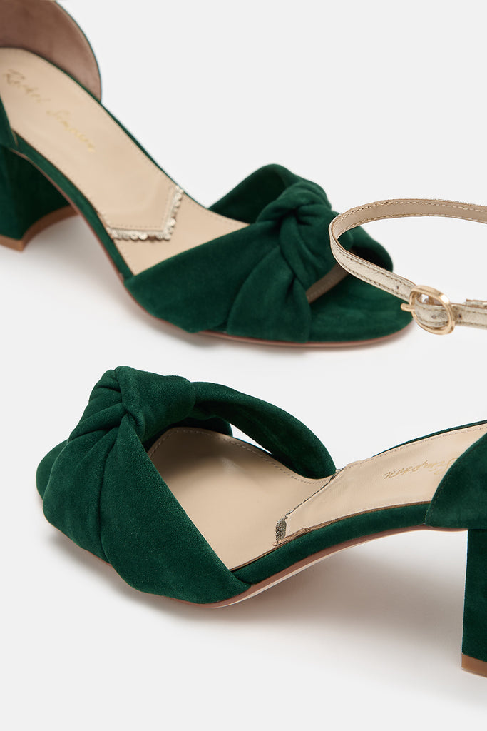 close up detail shot of a pair of forest green suede block heel shoes with knot detail and gold leather ankle straps