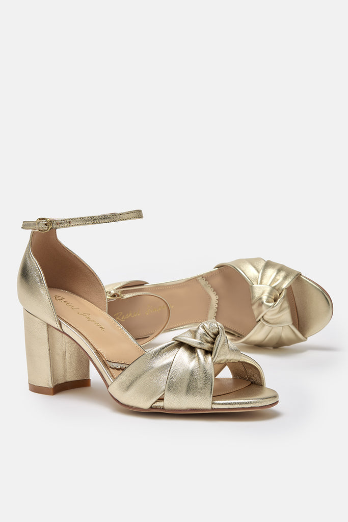 a pair of gold leather block heel occasion shoes with knot detail and ankle straps- one shoe is lying on its side
