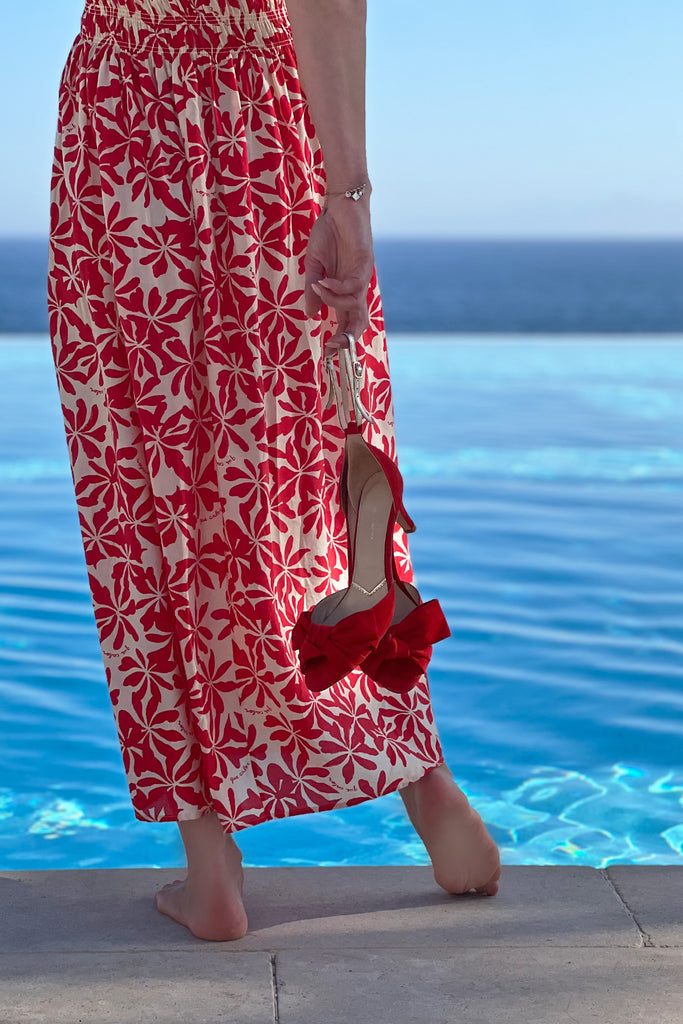 Person wearing a red and white patterned dress and red high-heeled shoes by a pool.