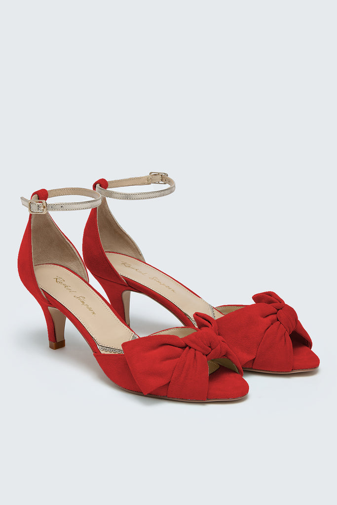 Red high-heeled shoes with bow detail on a light gray background