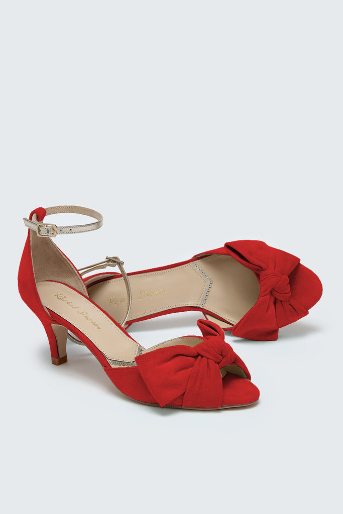 Red high-heeled shoes with bow details on a light gray background