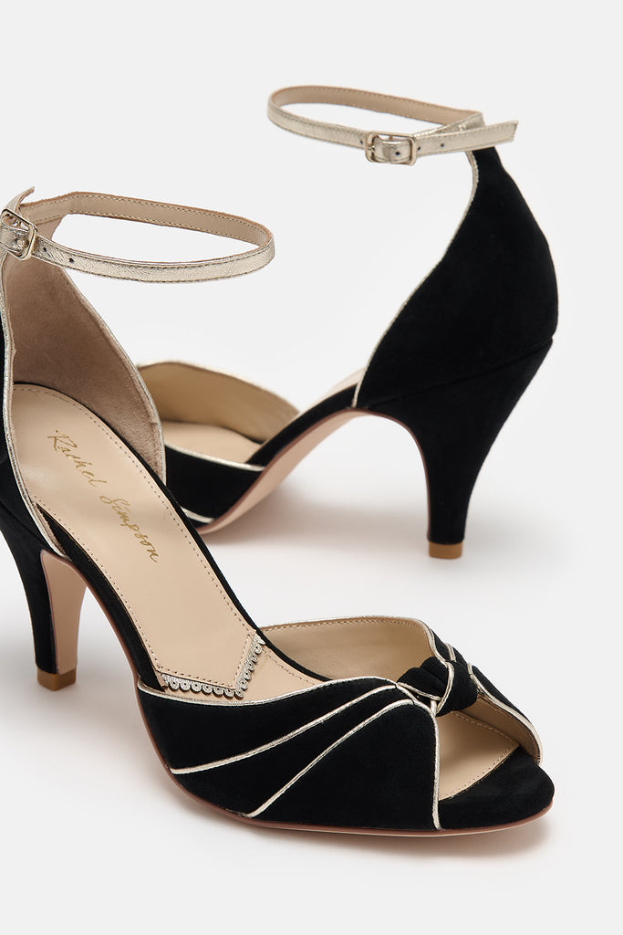 close up detail shot of a pair of black and gold suede occasion shoes with vintage inspired knot detail, mid heels and gold leather ankle straps