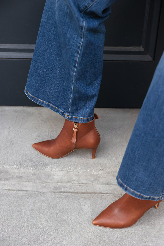 Brown pointed-toe high heels worn with blue jeans on a concrete floor.