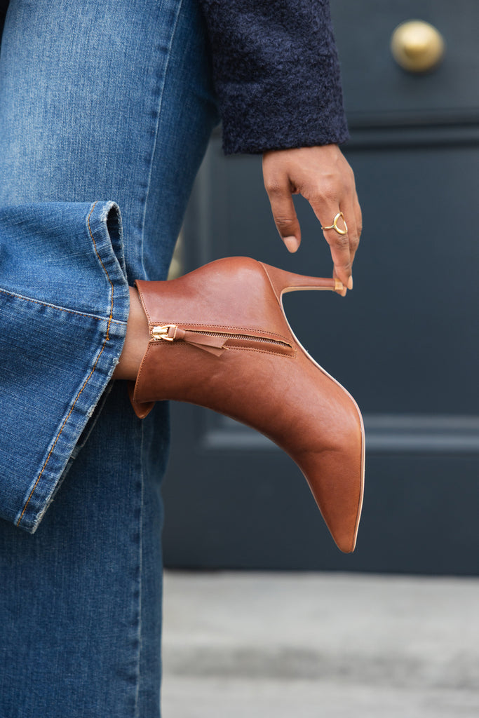 Brown ankle boot held by a person wearing blue jeans and a navy coat.