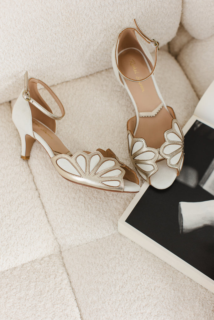pair of ivory suede and gold art deco vintage style wedding shoes, with low heels and ankle strap, on a cream sofa