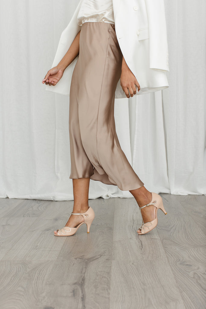 model in a gold satin skirt walking in a pair of blush pink nude and gold leather t-bar occasion shoes with mid heels and ankle strap