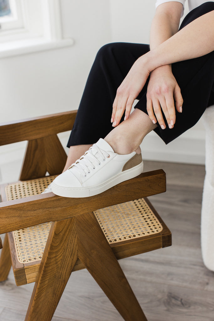 model wearing a white vegan leather trainer with her foot  resting on a chair